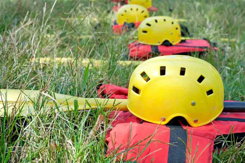 Capacetes amarelos, colete salva vidas e remos sobre a grama verde.