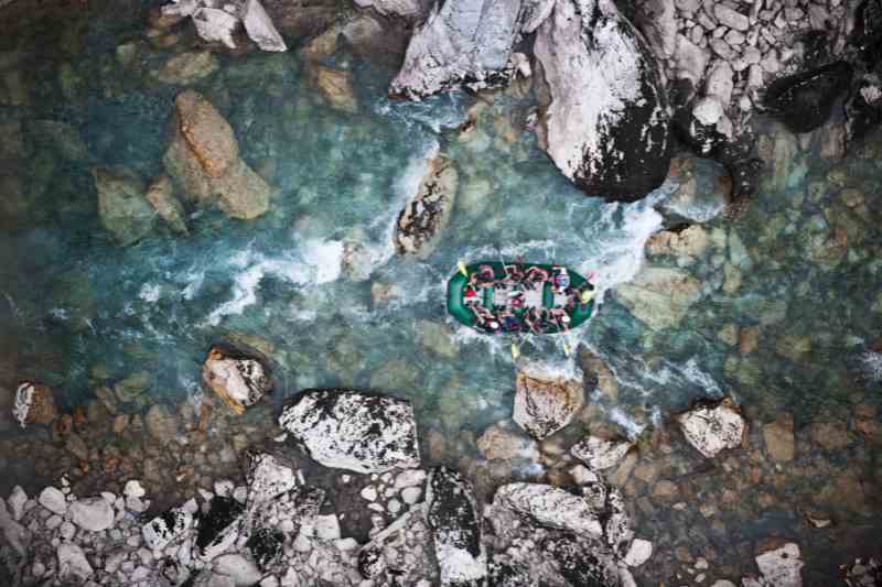 Bote navegando em rio de águas cristalinas com pedras grandes e pequenas. Imagem vista de cima.