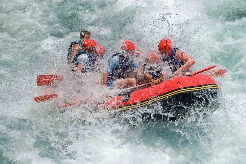 Pessoas praticando Rafting em botes vermelhos na água turbulenta.