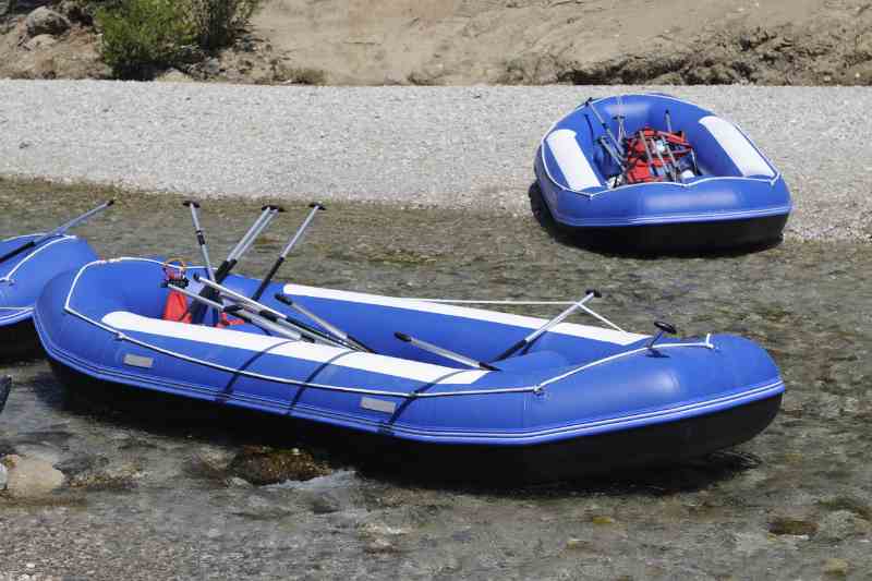 Dois botes infláveis azuis posicionados em uma área de rio raso com água clara e pedregulhos no fundo.