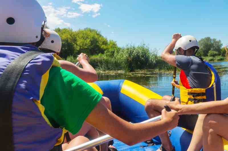Pessoas navegam em bote amarelo e azul em rio calmo envolto por vegetação.