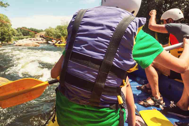 Praticantes de rafting descem rio turbulento e cheio de pedras com colinas e vegetação ao fundo.