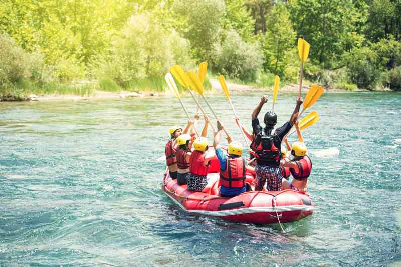 Praticantes de rafting levantam remo enquanto descem rio com aguas azuis.