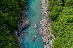 Pessoas praticando Rafting em dois botes vermelhos em um rio azul.