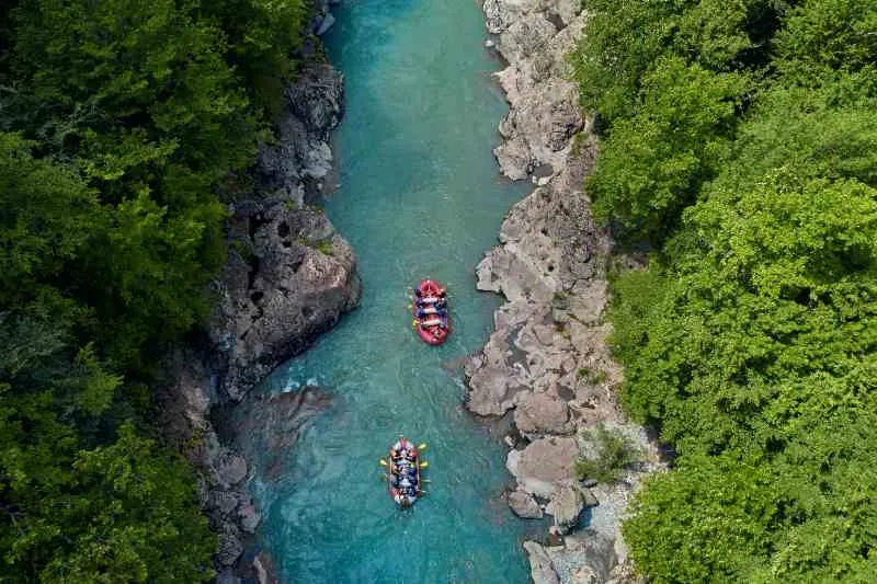 Pessoas praticando Rafting em dois botes vermelhos em um rio azul.