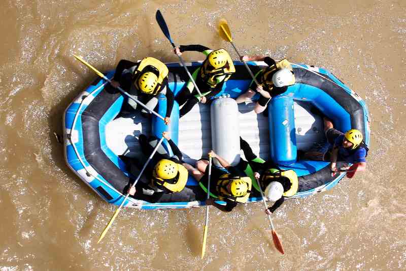 Visão aérea de um bote azul e preto, transportando um grupo de pessoas em um rio de águas turvas.