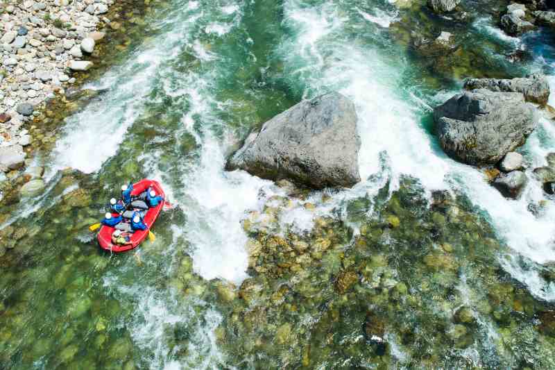 Bote desce rio de água cristalina. Nota-se a presença de pedras e pedregulhos.