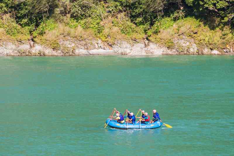 Praticantes de rafting remam sobre bote azul em rio de água azul turquesa.