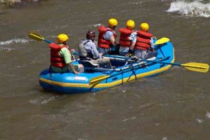 Bote azul , com cinco pessoas desce rio de águas escuras.
