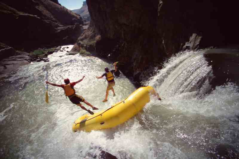 Praticantes de Rafting caindo do bote em queda d'água de um rio.