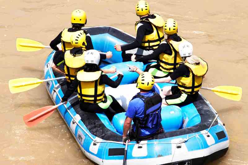 Sete pessoas em um bote azul sobre rio de águas escuras.