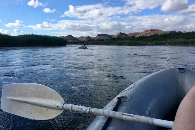 Foto retirada de dentro do bote. Pode-se ver o rio, o horizonte e o céu azul.