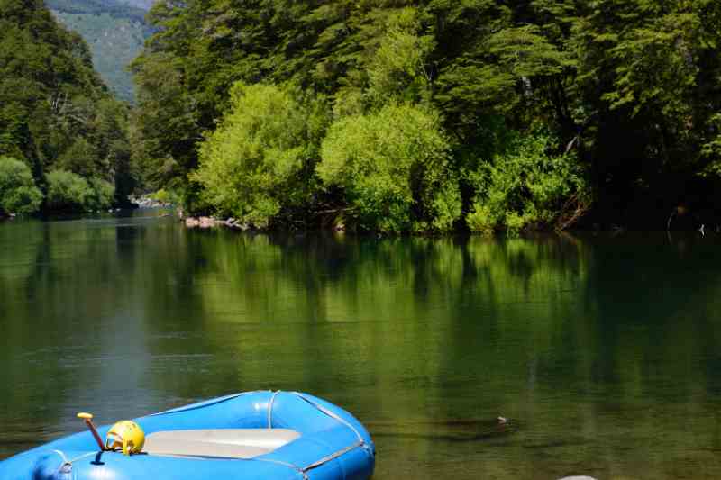 Bote azul sobre rio calmo de águas verdes, margeado por vegetação densa.