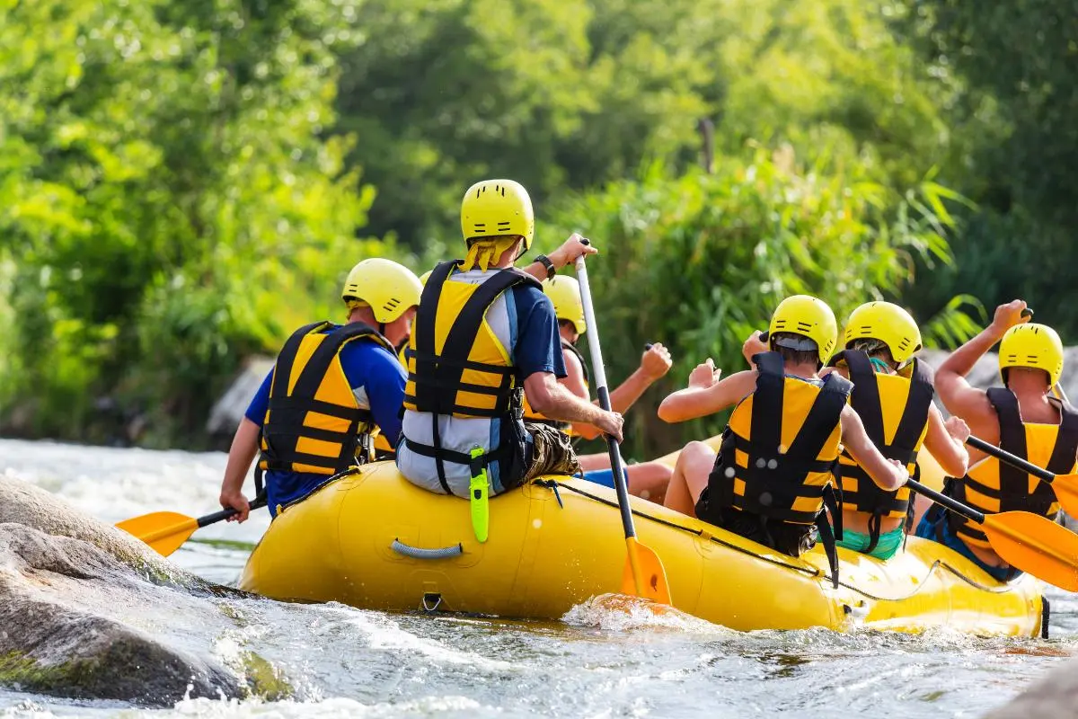 Grupo de pessoas praticando rafting em bote amarelo, remando juntos em um rio do Estado de São Paulo com corredeiras, cercado por vegetação verde.